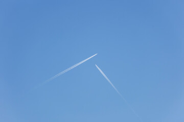 Two airplanes flying towards each other at right angles in a blue sky
