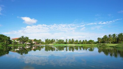 A beautiful lake on a golf course in the Dominican Republic. Green meadow grass background for palms and trees. The blue sky is reflected in the water on a sunny morning.