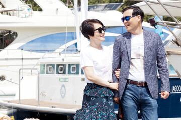 A middle aged couple walking while talking in front of a yacht
