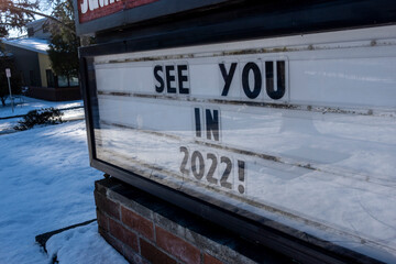 Angled view of a school changeable letter sign on a snowy day that says See You in 2022!
