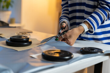 Tailor designer cutting fabric with old scissors and weights. Creative sewer working on new fashion clothes collection in studio. Workplace of clothing manufacture and craft production. Small business