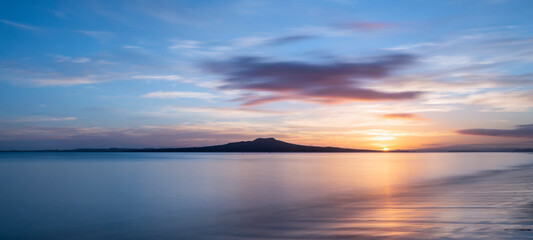 Naklejka na ściany i meble Sun rising over the Rangitoto Island at Milford Beach, Auckland.