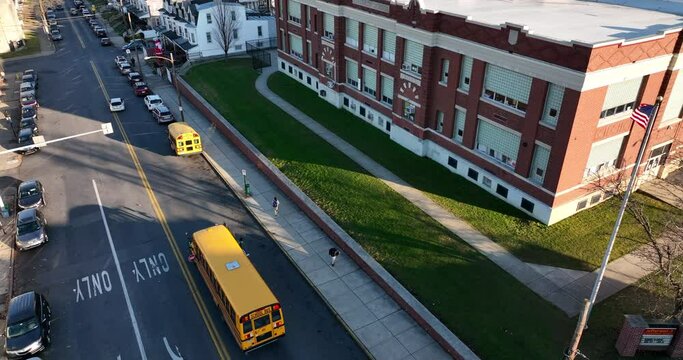 Students exit school bus at exterior of school building. Aerial drone view in urban city in USA. American town. Public education theme in America.