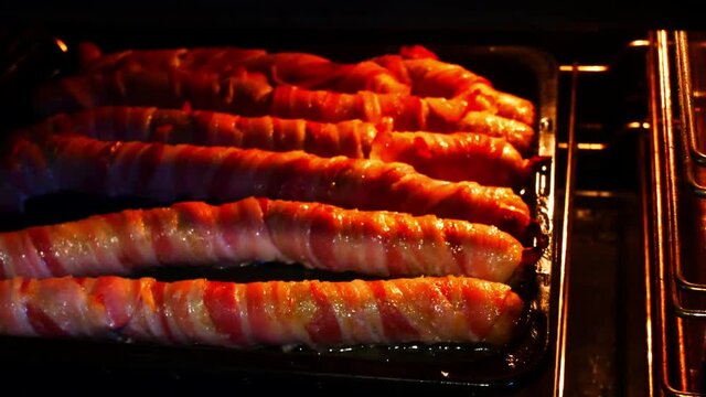 Opening oven to reveal sizzling extra long pigs in blankets bacon wrapped roasted party food close up sliding left shot