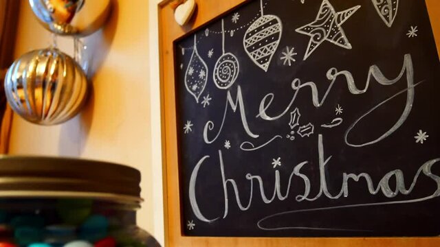 Merry Christmas and baubles decoration hand drawn on chalk blackboard hanging on kitchen wall dolly right
