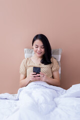 Young woman relaxing in bed while holding cell phone