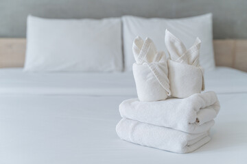 Fototapeta na wymiar Folded up soft white towels setup on white bed in a clean and comfortable bedroom of a hotel to welcome guests