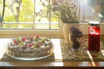 bouquet of summer flowers and berry pie with fresh raspberries, currants, mint and cream close-up on a windowsill in a private house