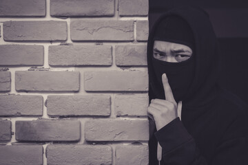 Thief wear cover faces and black jacket is hiding behind the old wall.
