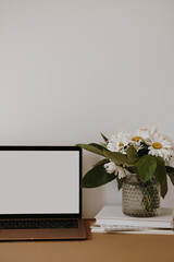 Laptop computer with blank screen on table with chamomile flowers bouquet. Aesthetic influencer styled workspace interior design template with mockup copy space