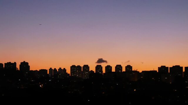 Silhouettes Of High-Rise Buildings At Sunset With Clear Skies And An Airplan