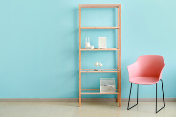 Wooden shelving unit with decor and pink armchair near blue wall