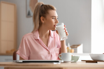 Fototapeta premium Pretty young woman drinking milk in kitchen