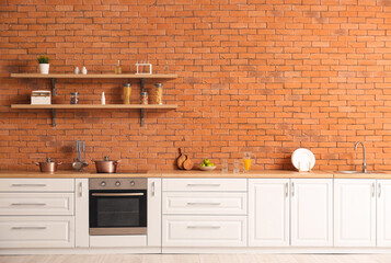 Interior of modern kitchen with white counters and brick wall
