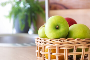 Wicker basket with apples on table top in kitchen, closeup