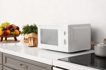 Modern microwave oven and food on counter near light wall