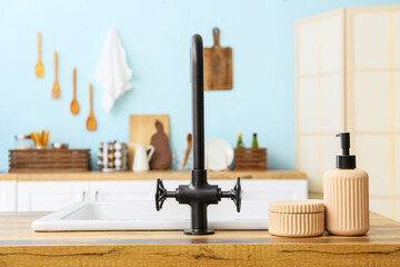 Black faucet and dishwashing detergent on wooden table top in kitchen