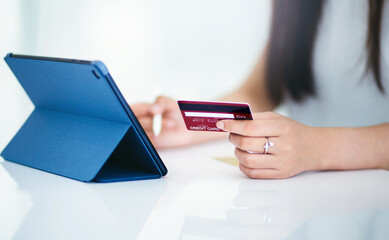 Focus in hand, young asian woman holding mockup of credit card and using digital tablet shopping or working online
