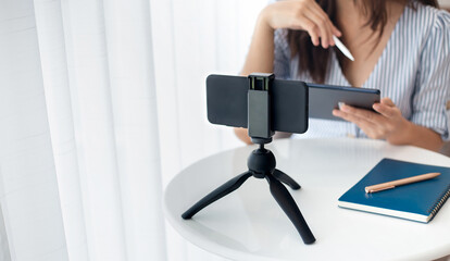 Young asian woman using mobile phone on small tripod live streaming to working or study online, concept working with new normal and social distancing