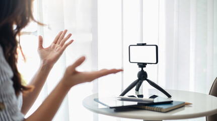 Young asian woman using mobile phone on small tripod live streaming to working or study online, concept  working with new normal and social distancing