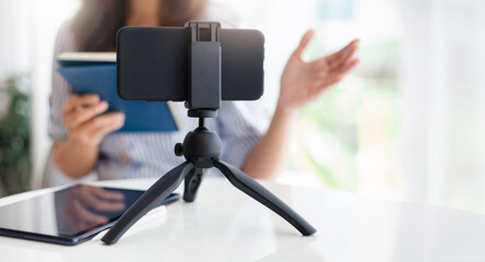 Young asian woman using mobile phone on small tripod live streaming to working or study online,...
