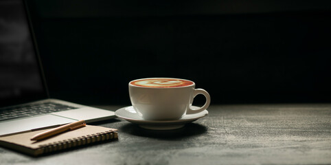 Work from home concept. desk office with laptop, notepad and, coffee cup and pen on table. dark tone and vintage style background