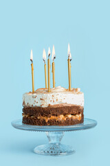 Stand with tasty birthday cake and burning candles on blue background