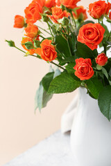 Vase with beautiful orange roses on table against beige wall, closeup