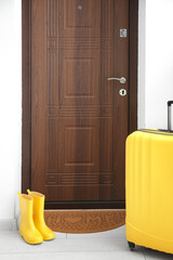 Brown mat with gumboots and suitcase near dark wooden door