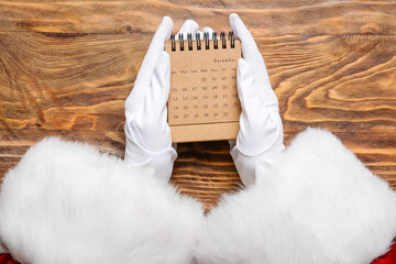 Santa Claus holding craft calendar on wooden background