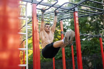 Fototapeta premium Athletic male athlete with a naked torso trains the abdominal muscles by lifting his legs up on workout ground. Outdoor workout
