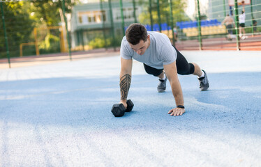 Athletic man doing dumbbell push-ups in the stadium