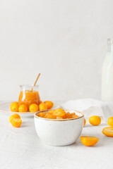 Bowl of tasty kumquat jam and fresh fruits on light background