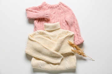 Knitted children's sweaters and reed flowers on white background