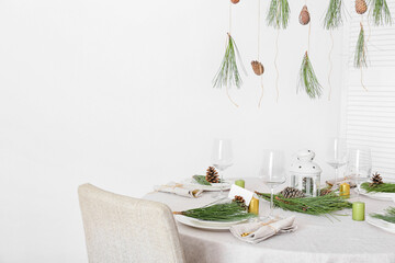 Beautiful table setting with pine cones and fir branches near white wall