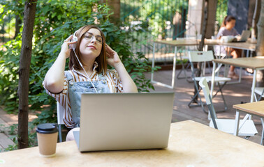 Young pretty woman with laptop listen music in headphones at outdoor coworking space