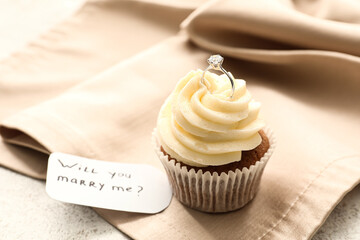 Tag with text WILL YOU MARRY ME, cupcake and engagement ring on napkin