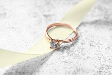 Golden engagement ring with ribbon on grunge background, closeup