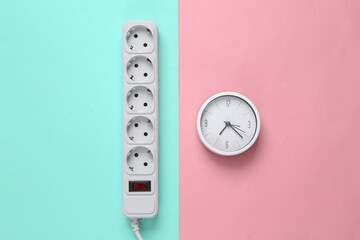 Electrical Extension cord and clock on a blue-pink pastel background. Top view. Flat lay