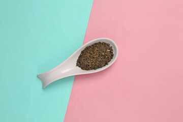 Ceramic spoon with dry green tea on blue-pink background. Top view