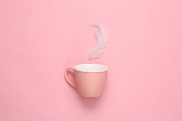 Teacup with feather on pink pastel background. Minimal layout
