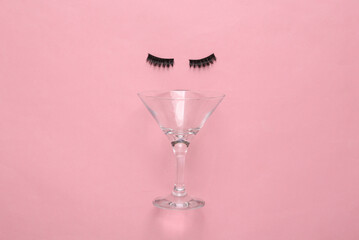 Creative layout. Face made of false eyelashes and cocktail glass on pink background. Top view
