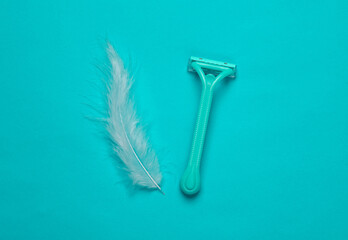 Depilatory razor and feather on a turquoise background. Top view