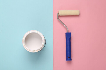 Obraz premium Paint roller and a can white paint on pink blue background. Top view. Home renovation concept