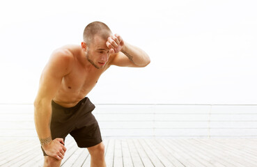 Obraz premium Tired male bodybuilder with a naked torso wipes sweat from his forehead after a hard workout on the beach