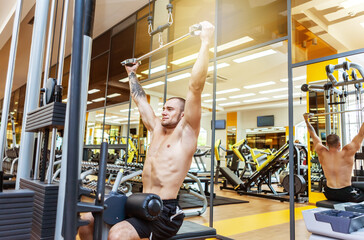 Fitness muscular man with naked torso working out in lat pulldown exercise machine in gym
