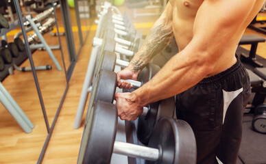 Fototapeta na wymiar Male bodybuilder holding dumbbells on a rack in the gym