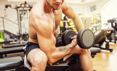 Fototapeta na wymiar Muscular man training biceps with concentration while sitting on bench in gym