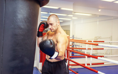 Muscular man with a naked torso in boxing gloves boxing a punching bag