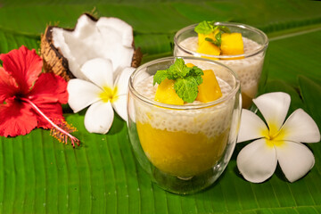Tropical tapioca and coconut cream with mango dessert on green banana leaf background  frangipani and hibiscus flowers.